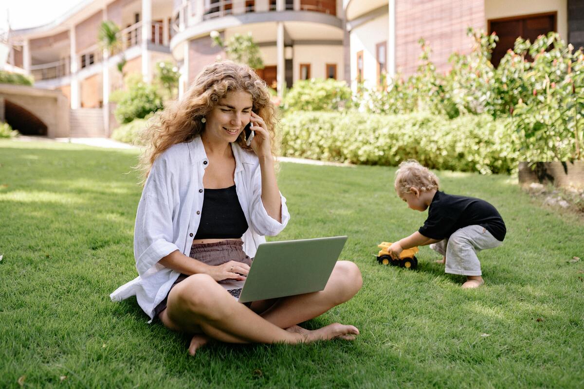 A woman seated on a grass while using a laptop