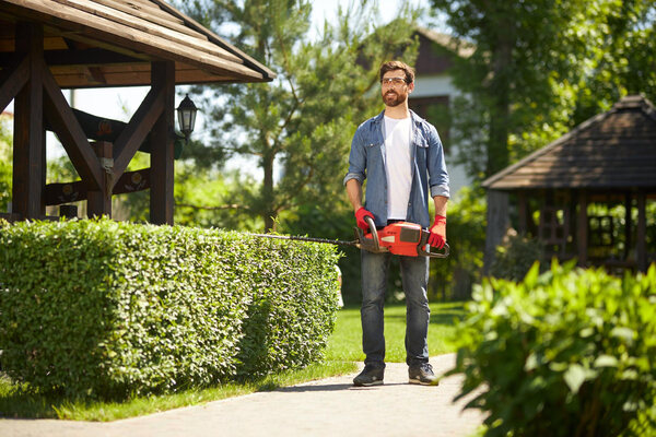 Man trimming hedge in garden with electric hedge trimmer.